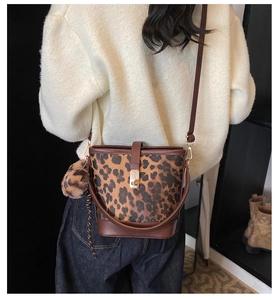 Leopard print bucket bag detail showing plush pom-pom charm and golden metal clasp