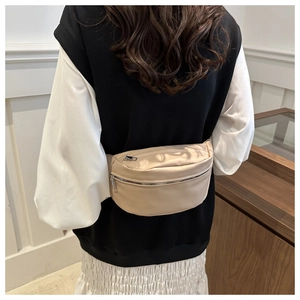 Close-up of beige nylon crescent waist bag worn as a crossbody with silver zipper detail