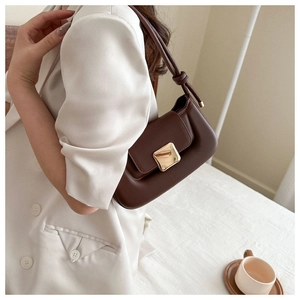 Détail du sac baguette en cuir marron foncé avec boucle dorée et bandoulière nouée