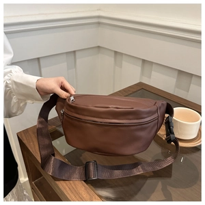 Detail of a dark brown leather waist bag with adjustable nylon strap on a wooden table