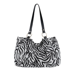 Large zebra print tote bag with black leather handles and gold rings on white backdrop
