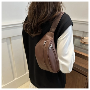 Detailed back view of a brown leather crossbody chest bag worn by a person in a minimalist room