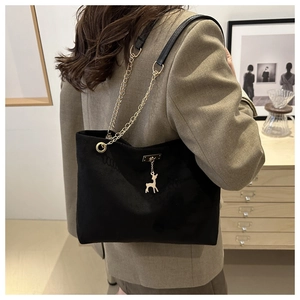 Detail of black suede tote bag with golden deer charm and chain strap shown on model