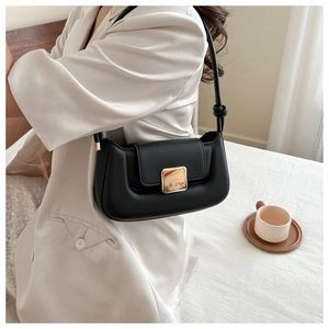Détail d'un sac baguette noir avec boucle dorée et bandoulière fine avec décoration de nœud