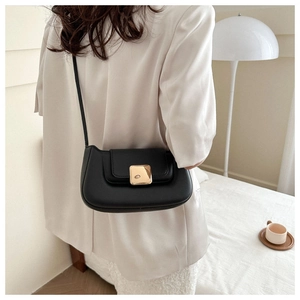 Détail du sac baguette noir mat avec boucle dorée porté par un mannequin dans un décor épuré