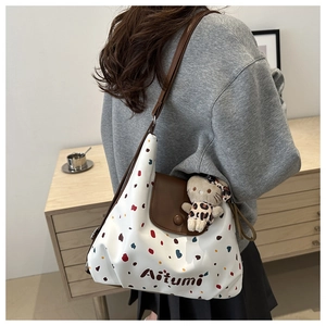 Dettaglio laterale della borsa tote a pois con patta in pelle marrone e charm a gatto