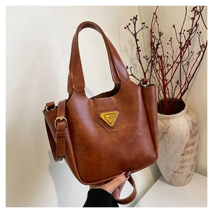 Detail of vintage brown leather bag showing gold metal logo and adjustable shoulder strap