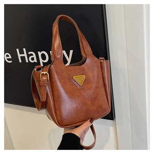 Detail of a brown vintage PU leather tote bag with a golden triangular logo and sleek handle