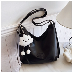 Detail of large black leather hobo bag featuring a cute white cloud plush pendant