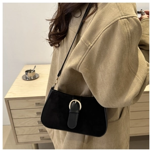 Close-up of minimalist black shoulder bag with a gold round buckle on a model