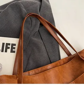 Detail of the brown faux leather tote bag showing lychee texture and long smooth straps