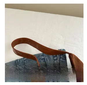 Detail of blue denim tote bag with brown faux leather handle and white stitching