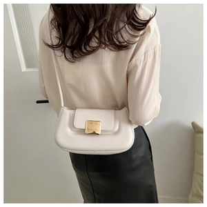 Détail du sac baguette crème avec boucle dorée porté par un mannequin stylé