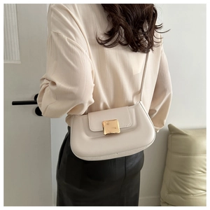 Détail d'un sac baguette beige minimaliste avec boucle dorée porté à l'épaule par le mannequin