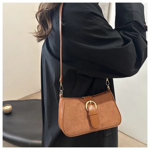 Detail of vintage brown shoulder bag with golden ring buckle worn over a black coat