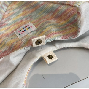 Dettaglio della texture in maglia arcobaleno con bottone a pressione e etichetta