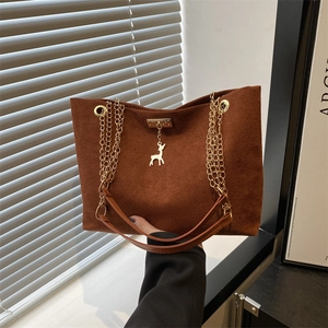 Brown suede tote bag with gold deer pendant and chain strap in natural sunlight