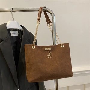 Brown suede tote bag with deer charm and gold chain strap hanging next to grey blazer