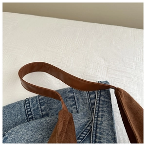 Close-up of blue denim tote bag with brown leather strap and suede stitching detail