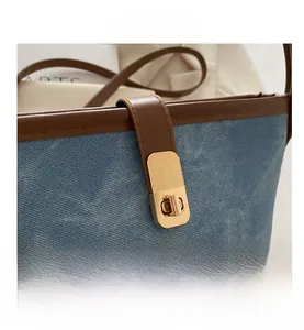 Close-up of golden turn-lock closure on blue denim bucket bag with brown leather trim