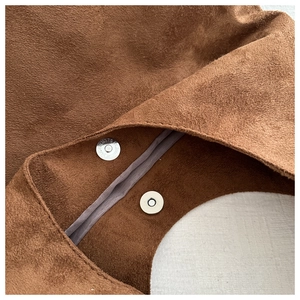 Detail view of magnetic metal clasp closure and interior lining on a brown suede tote bag