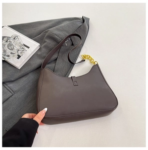 Detail einer dunkelbraunen Hobo-Tasche aus Kunstleder mit goldener Kette auf Sakko