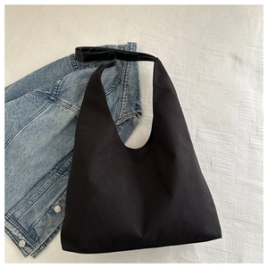 Detailed view of black canvas hobo bag with leather strap on white textured fabric