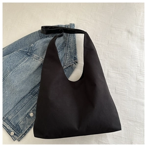 Top view of a minimalist black fabric tote bag on denim jacket and white quilted fabric
