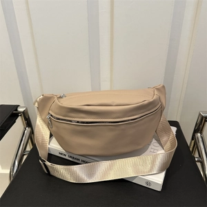 Minimalist beige PU leather crossbody waist bag with wide fabric strap on a book