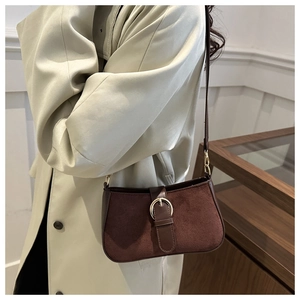 Detail of dark brown matte shoulder bag with gold buckle on a beige trench coat