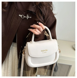 Close-up of cream leather saddle bag featuring gold fashion lettering and round handle