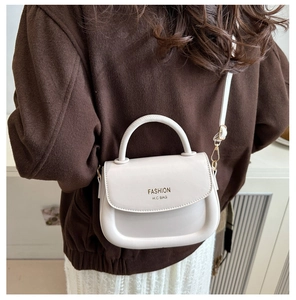 Detail of a minimalist cream saddle bag featuring elegant Fashion H.C gold lettering