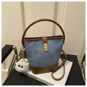 Detail of a denim blue bucket bag with brown trim and plush charm on a chair