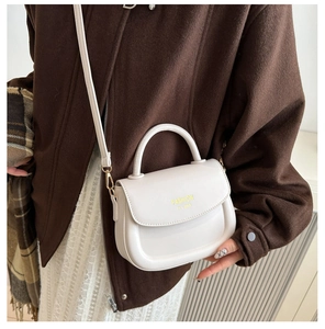 Detailed view of cream PU leather saddle bag with top handle and gold hardware on model