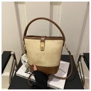 Detail of color-block bucket bag with gold metal twist lock and white plush pendant accessory