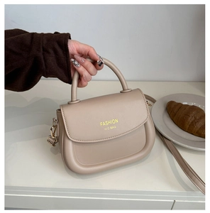 Chic beige saddle bag with adjustable strap shown next to a croissant and afternoon tea