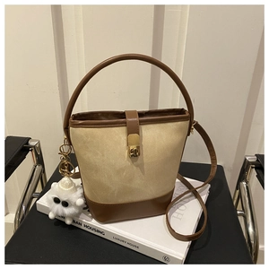 Detail view of a two-tone bucket bag with beige suede, brown leather and a plush charm