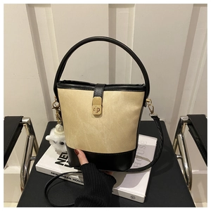 Detail of a contrast bucket bag with beige canvas body, black leather base, and gold hardware