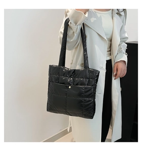 Detail of black quilted puffer tote bag with glossy finish and gold snap button pocket