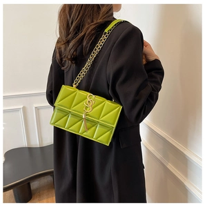 Detail of green quilted crossbody bag with gold chain and metal tassel on black blazer
