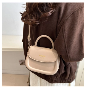 Detail of a beige fashion saddle bag with gold logo on a model with wool coat