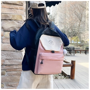 Close-up of color-block backpack showing smooth nylon texture and plush ball charm