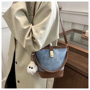 Detail of color-block bucket bag with gold clasp and plush pendant in lifestyle setting