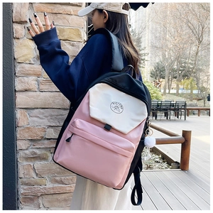 Outdoor view of a stylish pink and beige color-block backpack with a fuzzy pendant