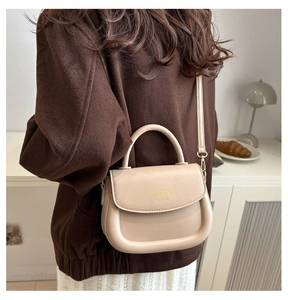 Close-up of cream saddle bag on model showing fine PU leather texture and gold lettering