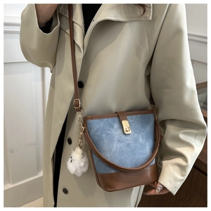 Close-up of blue canvas bucket bag with brown leather trim and golden twist lock detail