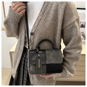 Detail of grey and black retro crossbody bag held by model wearing a knit cardigan