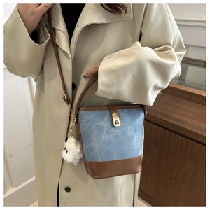 Detail view of blue bucket bag with brown leather trim and fluffy white doll charm