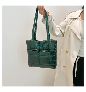 Detail of dark green quilted tote bag with metallic sheen and gold snap button pocket