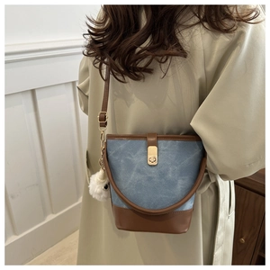 Detail of vintage denim bucket bag with brown leather trim worn with a khaki trench coat
